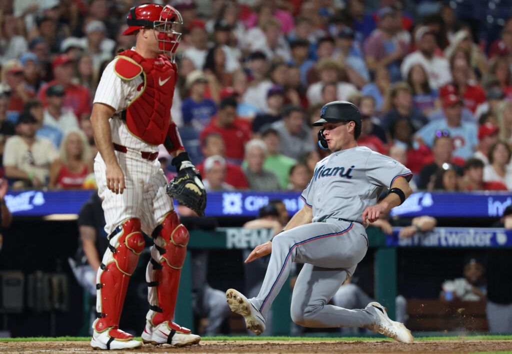 Aug 18, 2026; Philadelphia, Pennsylvania, USA; Miami Marlins right fielder Griffin Conine (18) scores past Philadelphia Phillies catcher J.T. Realmuto (10) during the eighth inning at Citizens Bank Park. Mandatory Credit: Bill Streicher-Imagn Images