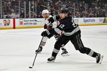 Dec 6, 2025; Los Angeles, California, USA; Los Angeles Kings left wing Trevor Moore (12) hits a slap shot against Chicago Blackhawks center Frank Nazar (91) during the second period at Crypto.com Arena. Mandatory Credit: Jonathan Hui-Imagn Images