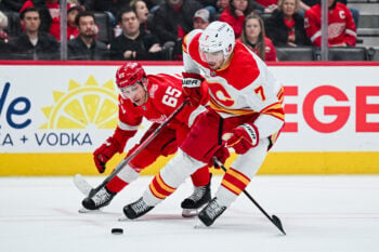 Mar 16, 2026; Detroit, Michigan, USA; Calgary Flames defenseman Kevin Bahl (7) and Detroit Red Wings right wing Dominik Shine (65) battle for the puck during the second period at Little Caesars Arena. Mandatory Credit: Tim Fuller-Imagn Images