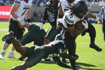 Oct 17, 2026; East Lansing, Michigan, USA;  Northwestern Wildcats running back Caleb Komolafe (5) scores while running through a tackle by Michigan State Spartans defensive back Jeremiah Favorite (24) during the second quarter at Spartan Stadium.  Mandatory Credit: Dale Young-Imagn Images