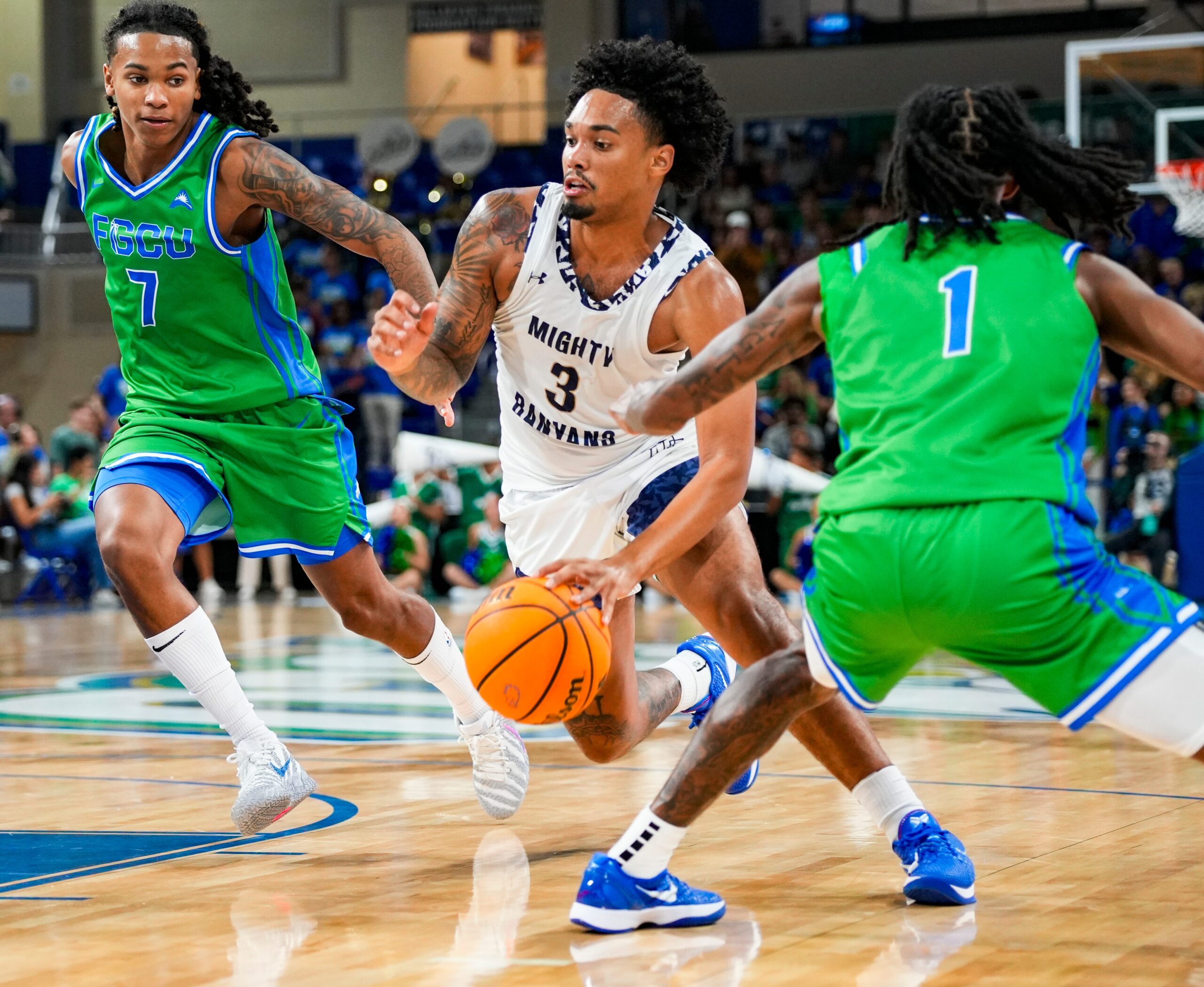 New College of Florida Mighty Banyans guard Adrian Moore (3) drives to the basket as Florida Gulf Coast Eagles guards Jordan Ellerbee (7) and Rahmir Barno (1) cover him during the first half of the season opener at Alico Arena in Fort Myers, Fla., on Monday, Nov. 3, 2025.