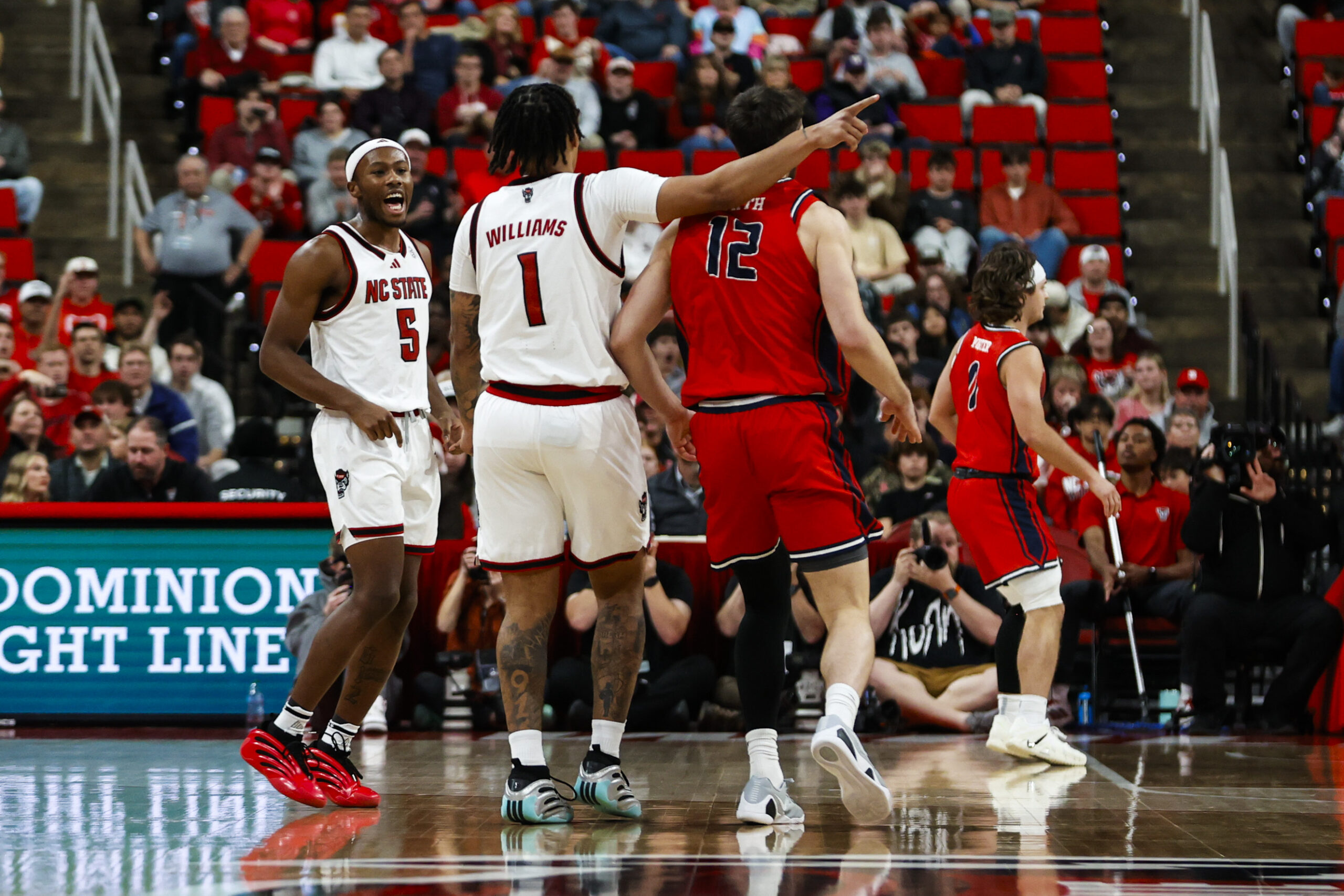 Dec 6, 2025; Raleigh, North Carolina, USA; NC State Wolfpack forward Darrion Williams (1) celebrates a three point shot over Liberty Flames forward Josh Smith (12) during the second half of the game at Lenovo Center. Mandatory Credit: Jaylynn Nash-Imagn Images