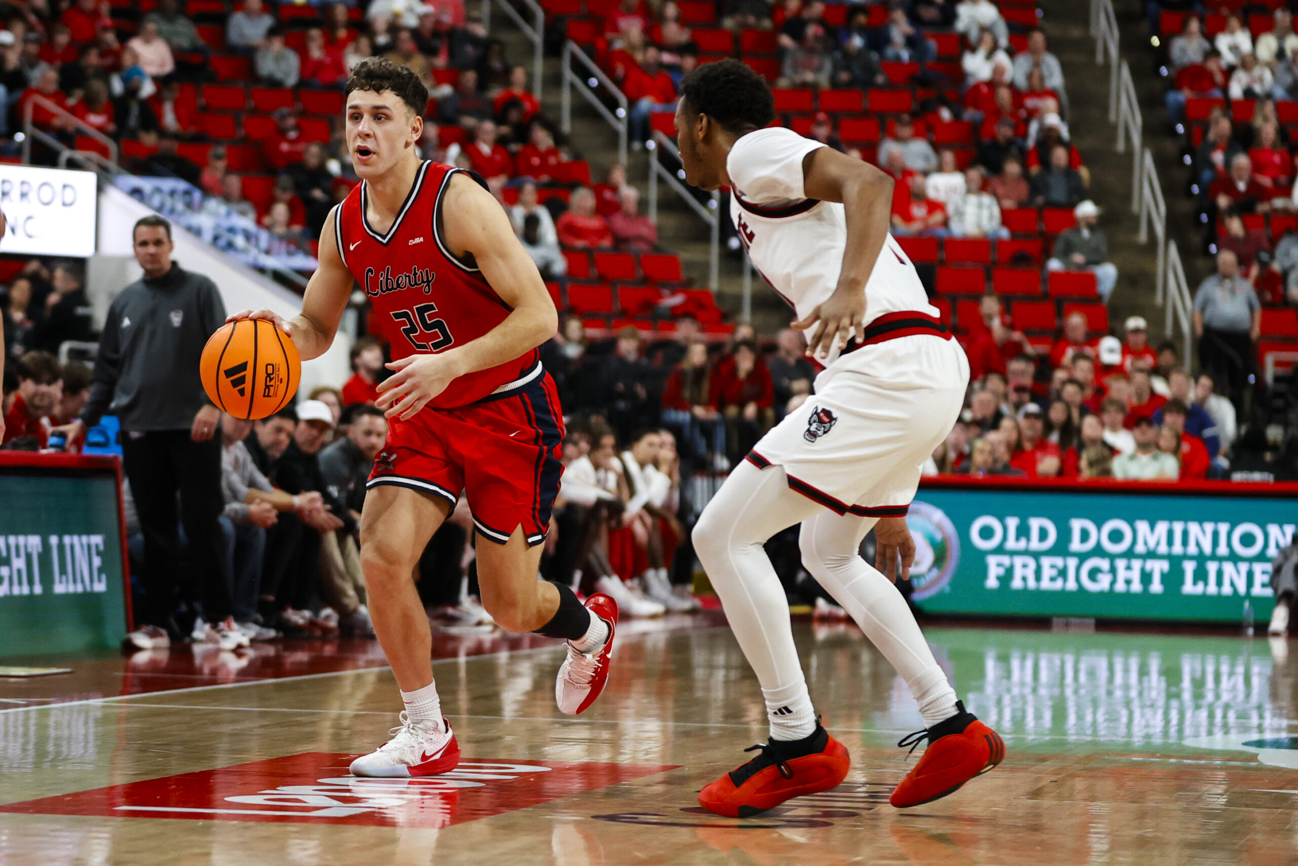 Dec 6, 2025; Raleigh, North Carolina, USA; Liberty Flames forward Zach Cleveland (25) dribbles the ball guarded by NC State Wolfpack guard Quadir Copeland (11) during the second half of the game at Lenovo Center. Mandatory Credit: Jaylynn Nash-Imagn Images