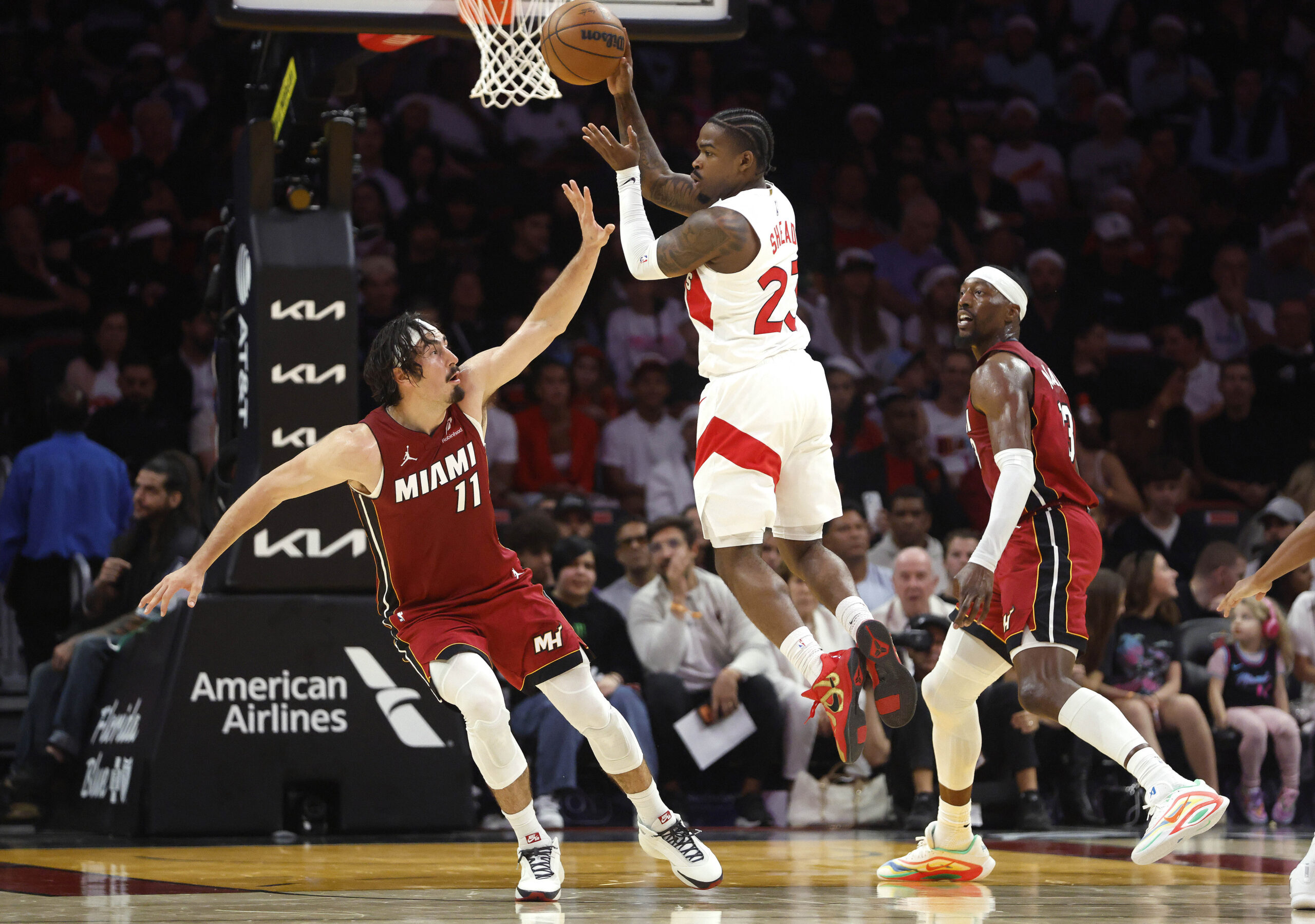 Dec 23, 2025; Miami, Florida, USA;  Toronto Raptors guard Jamal Shead (23) passes between Miami Heat forward Jaime Jaquez Jr. (11) and center Bam Adebayo (13) during the second half at Kaseya Center. Mandatory Credit: Rhona Wise-Imagn Images