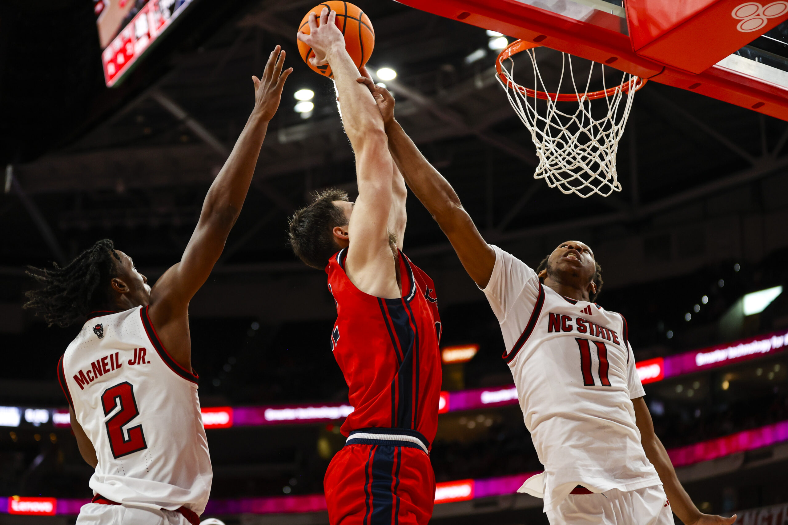 Dec 6, 2025; Raleigh, North Carolina, USA; Liberty Flames forward Josh Smith (12) attempts a dunk but is blocked by NC State Wolfpack guard Jr. Paul McNeil (2) and guard Quadir Copeland (11) during the second half of the game at Lenovo Center. Mandatory Credit: Jaylynn Nash-Imagn Images