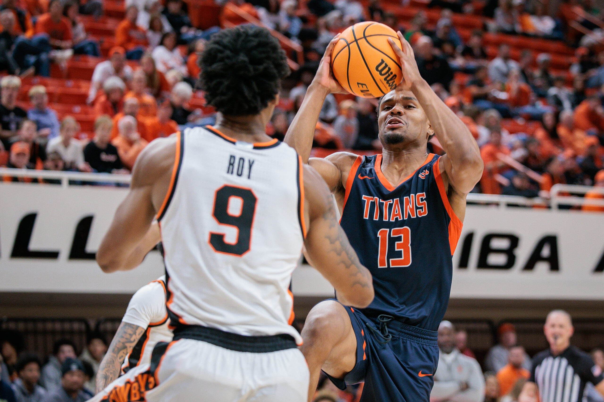 Dec 21, 2025; Stillwater, Oklahoma, USA; Cal State Fullerton Titans guard Jefferson de la Cruz Monegro (13) drives to the basket around Oklahoma State Cowboys guard Anthony Roy (9) during the second half at Gallagher-Iba Arena. Mandatory Credit: William Purnell-Imagn Images