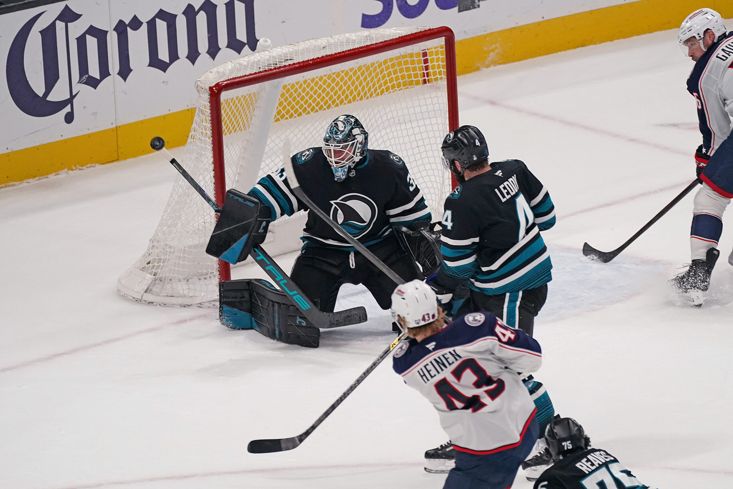 Jan 6, 2026; San Jose, California, USA;  San Jose Sharks goaltender Alex Nedeljkovic (33) makes a save against Columbus Blue Jackets left winger Danton Heinen (43) as San Jose Sharks defenseman Nick Leddy (4) helps defend in the third period at SAP Center at San Jose. Mandatory Credit: David Gonzales-Imagn Images